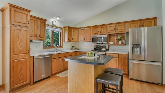 kitchen with lofted ceiling, stainless steel appliances, sink, a center island, and light wood-type flooring