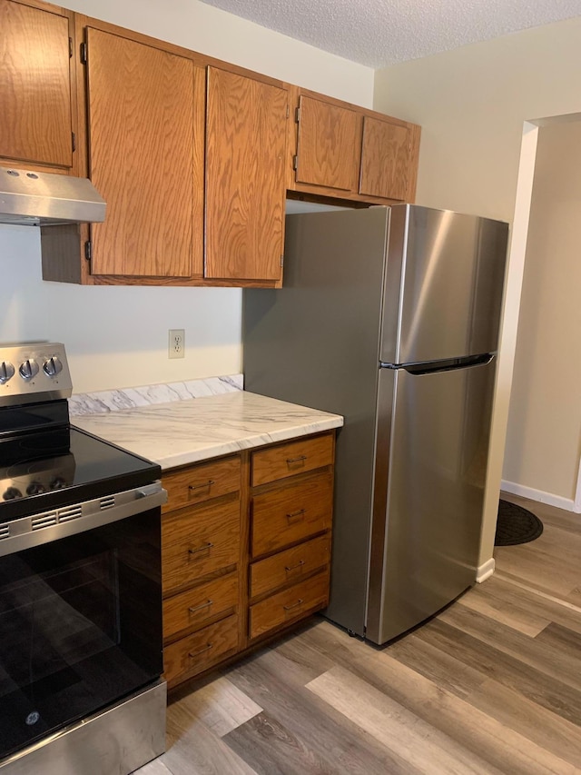 kitchen with light wood finished floors, range hood, a textured ceiling, light countertops, and appliances with stainless steel finishes