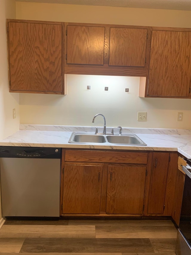 kitchen featuring brown cabinetry, light wood-style floors, a sink, and dishwasher