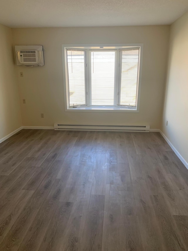 empty room with a wealth of natural light, baseboard heating, an AC wall unit, and dark hardwood / wood-style flooring