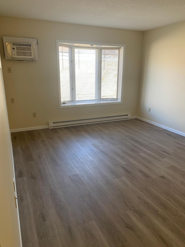 unfurnished room with a baseboard heating unit, a wall mounted AC, a textured ceiling, and dark hardwood / wood-style floors