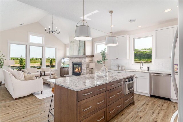 kitchen featuring appliances with stainless steel finishes, a stone fireplace, a wealth of natural light, light hardwood / wood-style floors, and white cabinetry