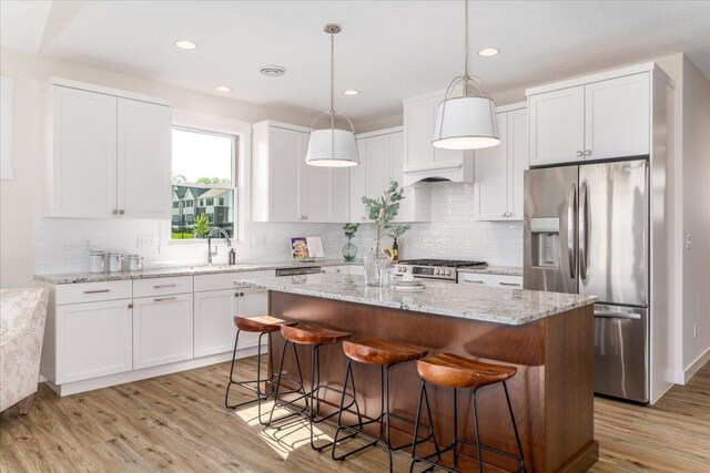 kitchen with stainless steel fridge with ice dispenser, a breakfast bar area, light hardwood / wood-style flooring, a kitchen island, and decorative backsplash