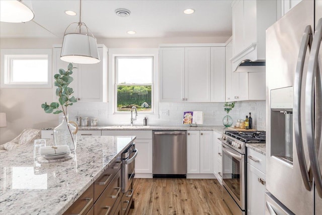 kitchen with sink, pendant lighting, stainless steel appliances, light stone countertops, and white cabinets