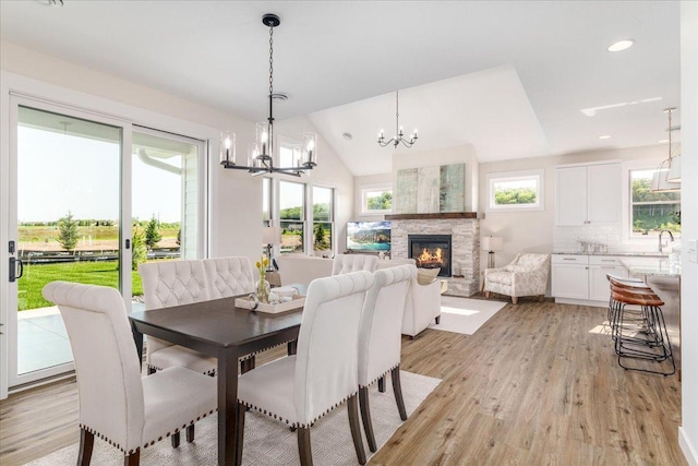 dining space featuring lofted ceiling, a stone fireplace, light hardwood / wood-style floors, and a healthy amount of sunlight