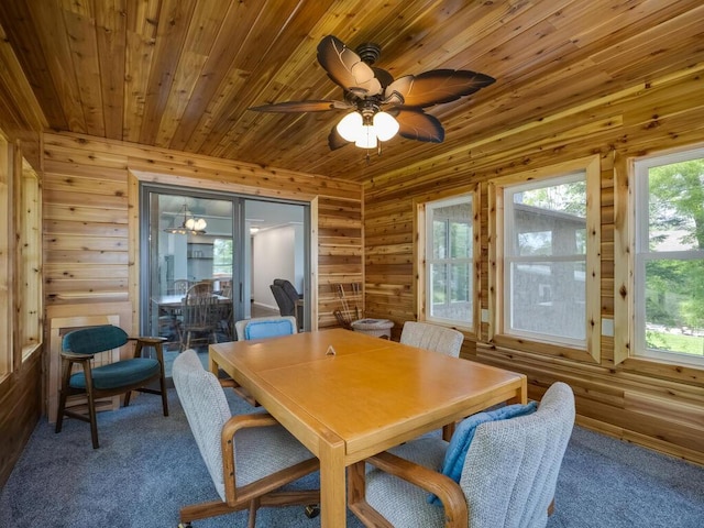 carpeted dining room with wooden ceiling, wooden walls, and a ceiling fan