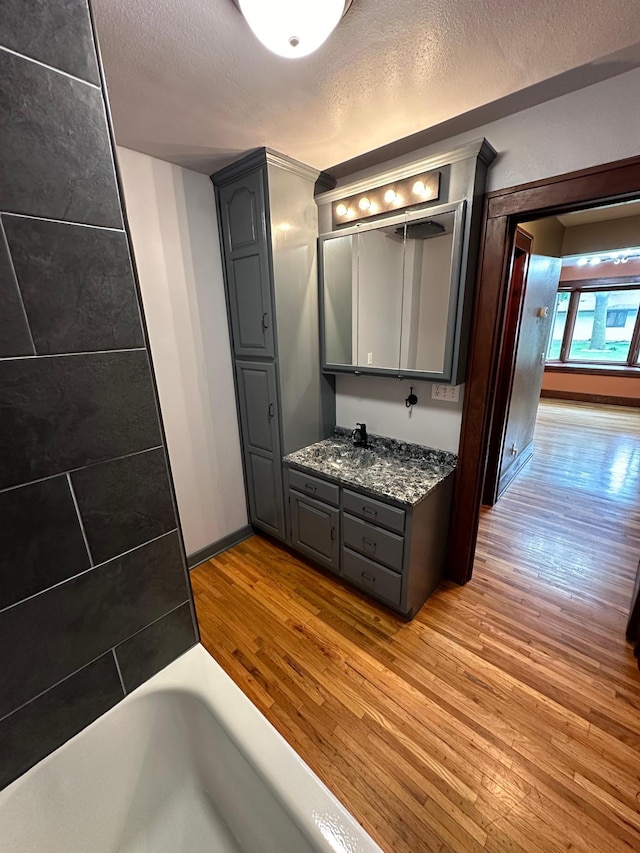 921 11th St N, Mountain Lake, MN 56159 - full bathroom with a textured ceiling, baseboards, a bath, vanity, and hardwood / wood-style flooring