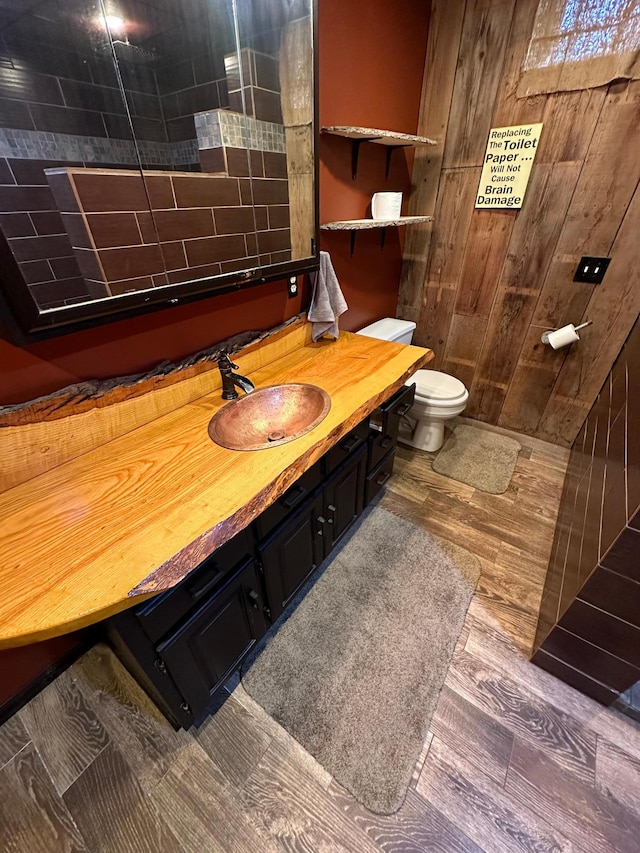 bathroom featuring vanity, wood walls, hardwood / wood-style floors, and toilet