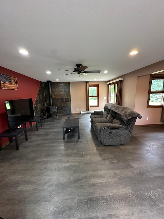 living room with ceiling fan, plenty of natural light, and a wood stove