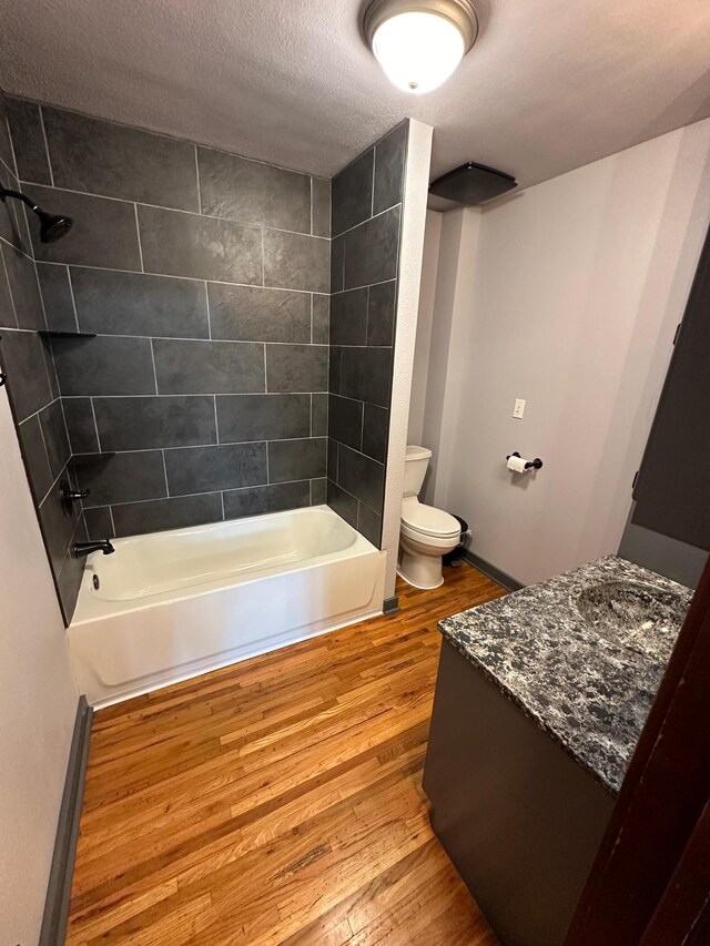 full bathroom with vanity, tiled shower / bath combo, a textured ceiling, hardwood / wood-style flooring, and toilet