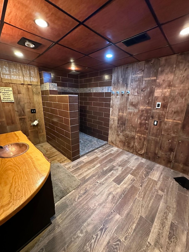 interior space featuring vanity, wood walls, walk in shower, wood-type flooring, and a paneled ceiling