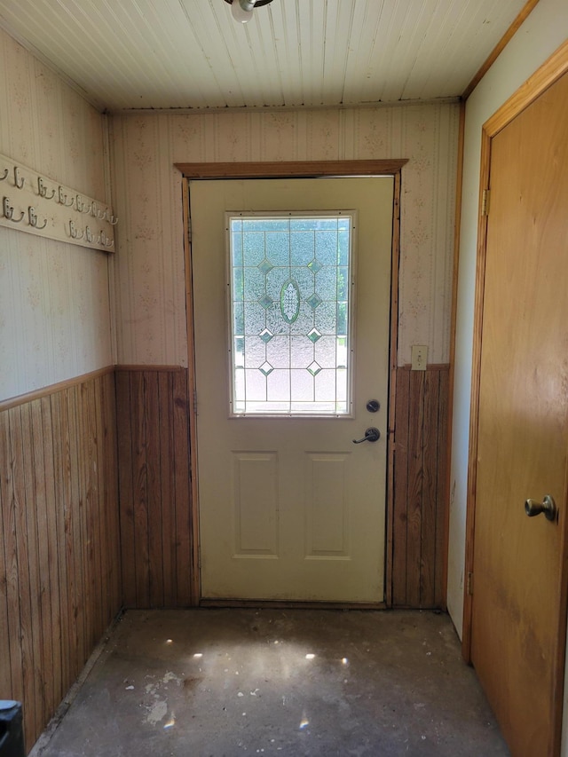 doorway to outside with concrete floors and wood walls