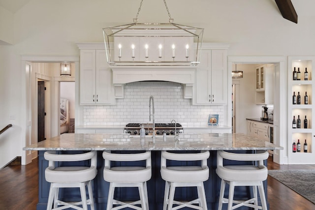 kitchen with a center island with sink, dark hardwood / wood-style floors, light stone countertops, and white cabinetry