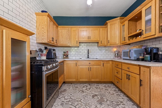 kitchen featuring light tile patterned floors, backsplash, stainless steel gas range, and sink