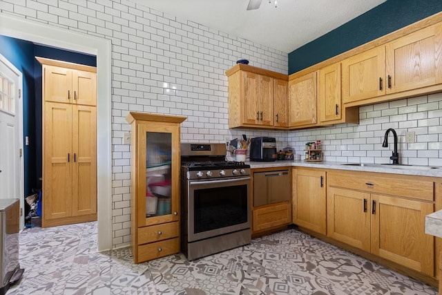 kitchen with light tile patterned flooring, sink, backsplash, stainless steel stove, and tile walls