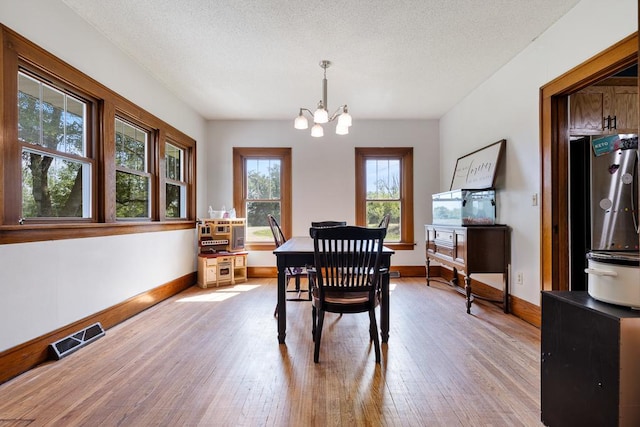 dining room with light wood-type flooring, a chandelier, and a textured ceiling