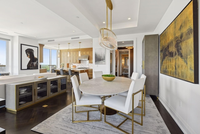 dining area with an inviting chandelier, dark hardwood / wood-style floors, and a raised ceiling