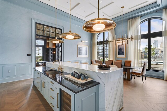 kitchen with a kitchen island with sink, white cabinets, dark parquet floors, sink, and decorative light fixtures