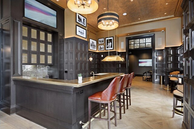 bar with hanging light fixtures, an inviting chandelier, a towering ceiling, light parquet flooring, and ornamental molding