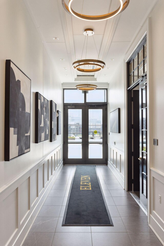 corridor with tile patterned floors, an inviting chandelier, french doors, and a tray ceiling