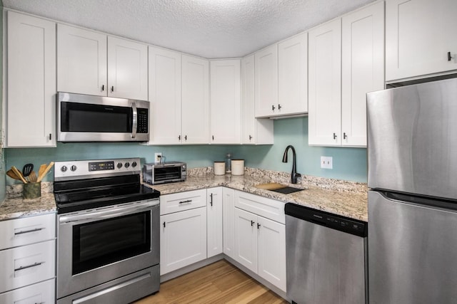 kitchen with stainless steel appliances, white cabinets, a textured ceiling, sink, and light wood-type flooring