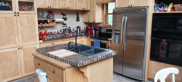 kitchen with light brown cabinetry, sink, tile counters, a kitchen island with sink, and black appliances