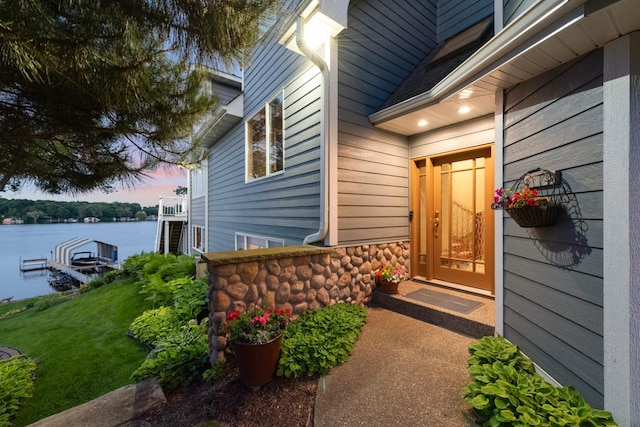 doorway to property featuring stone siding, a water view, and a yard