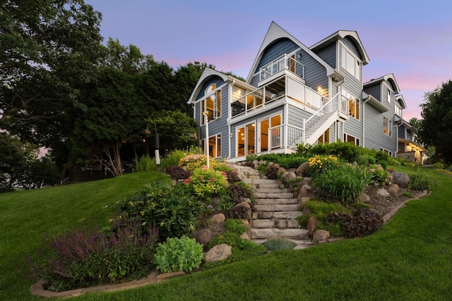 back of house at dusk featuring a balcony, stairs, and a lawn