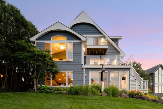 back of house at dusk featuring a yard, a balcony, and stairs