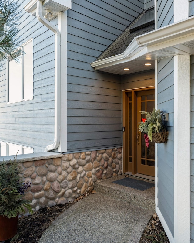 entrance to property featuring stone siding and roof with shingles