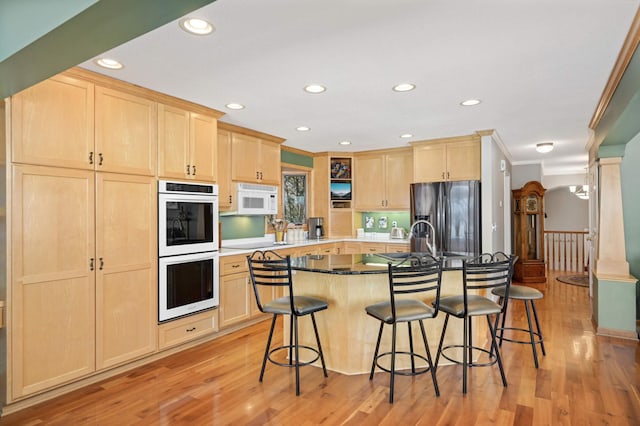 kitchen featuring white appliances, light wood finished floors, a breakfast bar area, light brown cabinets, and a sink