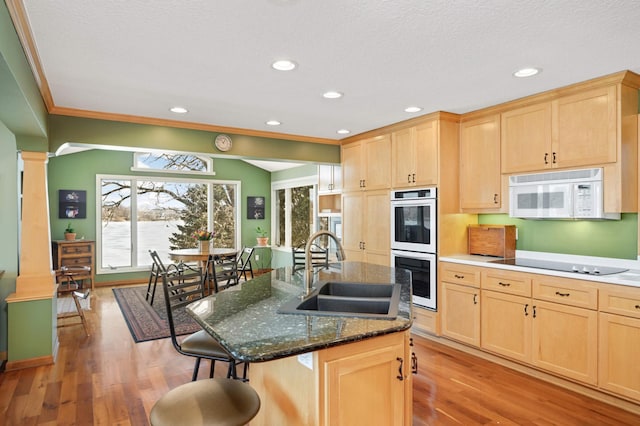 kitchen with a breakfast bar area, light brown cabinets, white appliances, a sink, and decorative columns