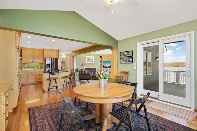 dining room with a fireplace, light wood finished floors, a ceiling fan, high vaulted ceiling, and ornate columns