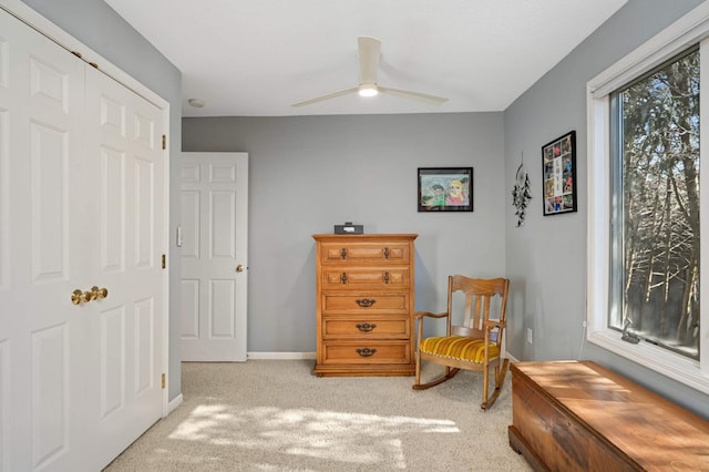 living area with a ceiling fan, light carpet, and baseboards