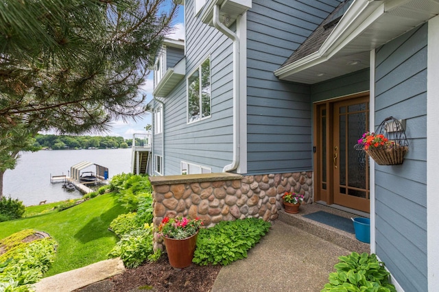 doorway to property with stone siding, a lawn, and a water view