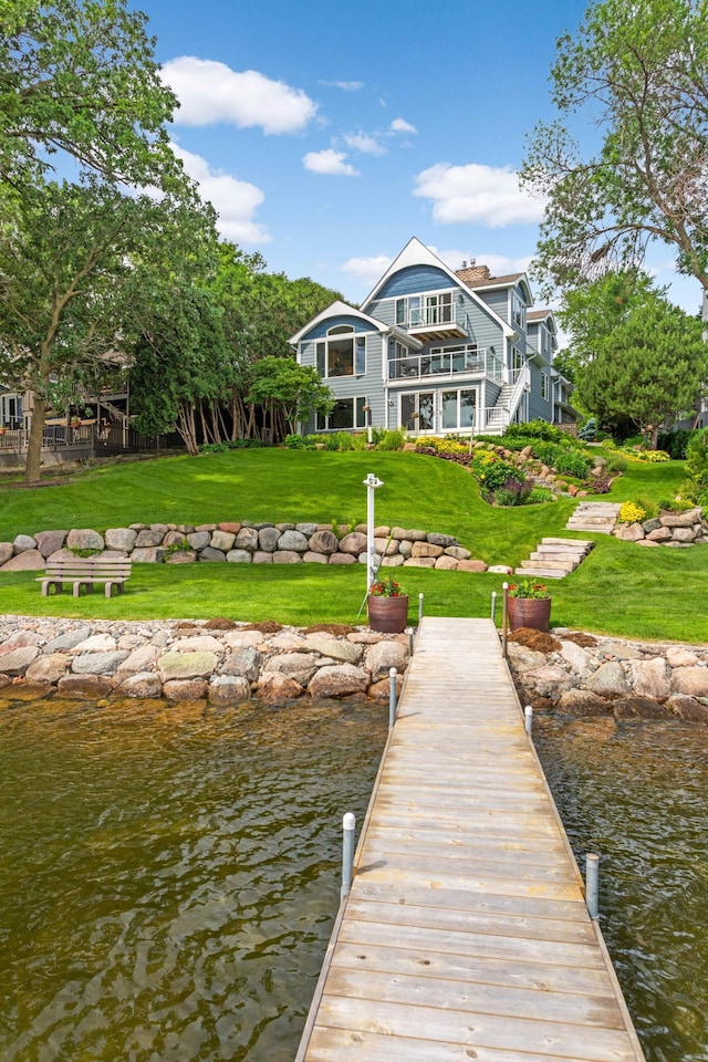 dock area featuring stairs, a lawn, a water view, and a balcony