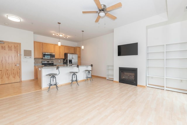 kitchen featuring a breakfast bar area, hanging light fixtures, light wood-type flooring, appliances with stainless steel finishes, and light stone countertops