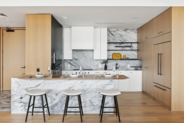 kitchen with white cabinetry, light hardwood / wood-style flooring, paneled built in refrigerator, decorative backsplash, and a breakfast bar