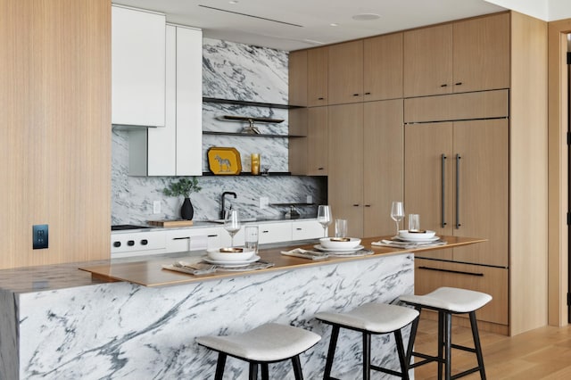 kitchen featuring backsplash, sink, white cabinets, light hardwood / wood-style floors, and a breakfast bar area