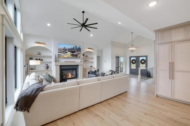 living room featuring french doors, built in shelves, ceiling fan, high vaulted ceiling, and light hardwood / wood-style flooring