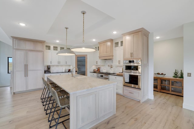 kitchen with decorative backsplash, light wood-type flooring, a center island with sink, and hanging light fixtures