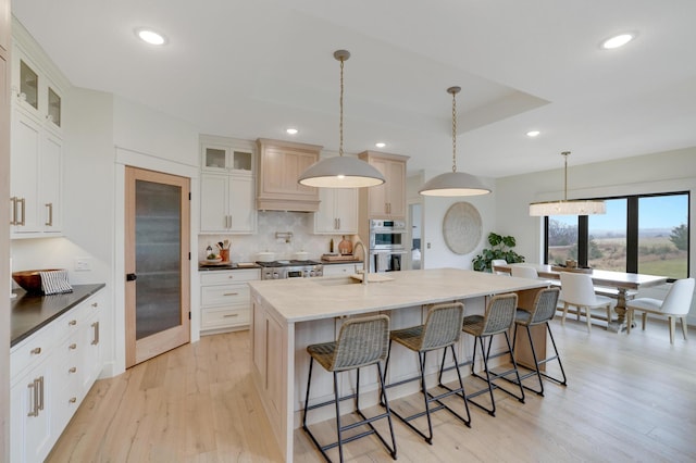 kitchen featuring sink, white cabinetry, a kitchen island with sink, and light wood-type flooring