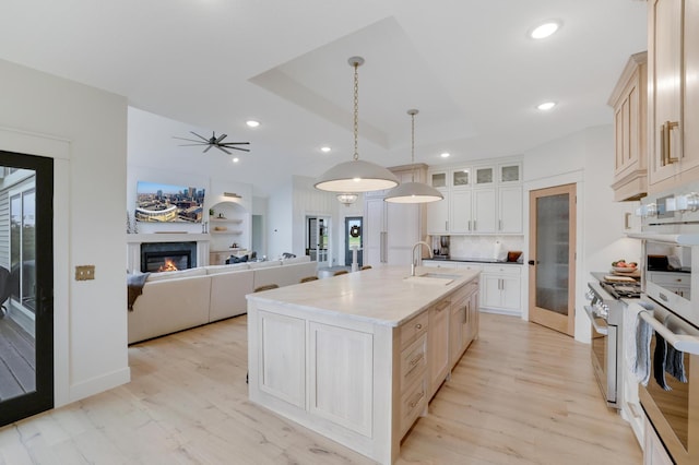 kitchen featuring sink, backsplash, decorative light fixtures, a center island with sink, and light wood-type flooring