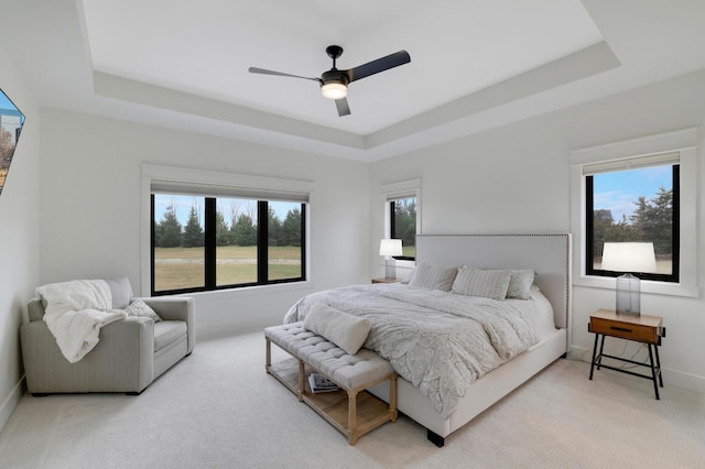 bedroom featuring light colored carpet, a raised ceiling, multiple windows, and ceiling fan