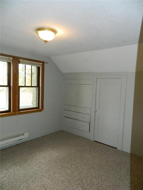 additional living space with carpet flooring, a baseboard radiator, a textured ceiling, and lofted ceiling