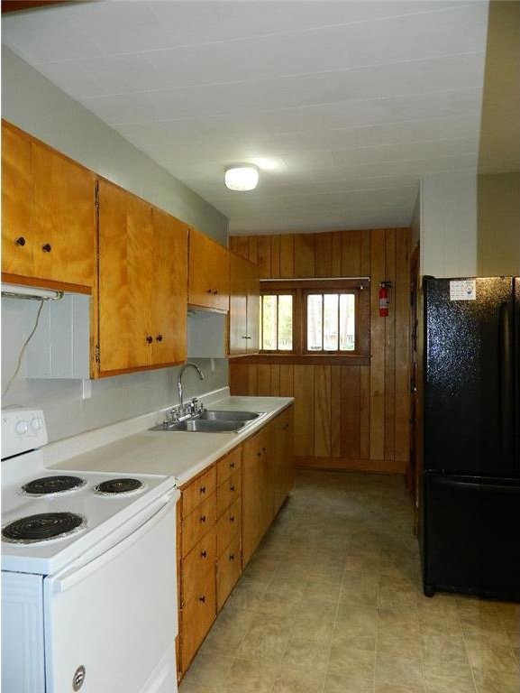 kitchen with white electric range, wood walls, black refrigerator, sink, and light tile floors