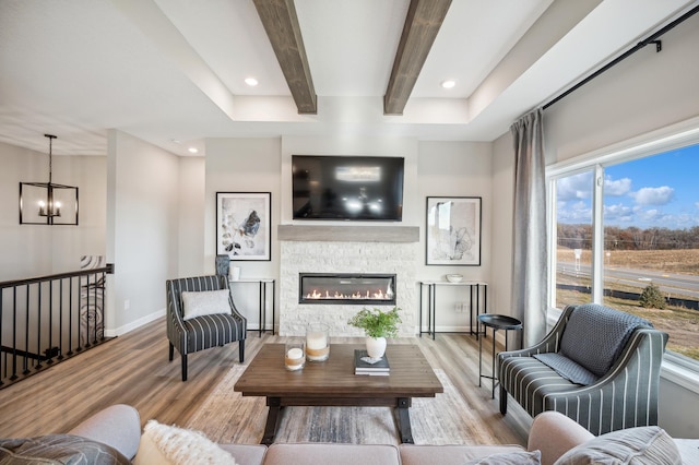 living room featuring a fireplace, beam ceiling, a chandelier, and light hardwood / wood-style flooring