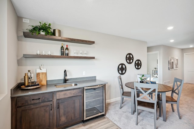 bar with sink, beverage cooler, dark brown cabinets, and light hardwood / wood-style flooring