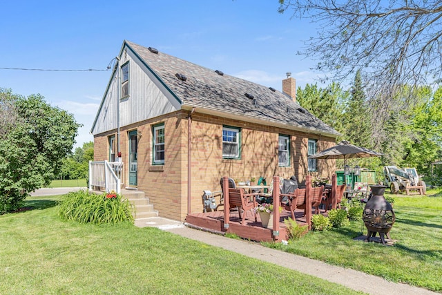 rear view of house with brick siding, a wooden deck, an outdoor fire pit, a chimney, and a yard