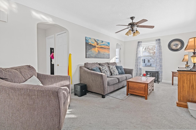 living area with baseboards, arched walkways, ceiling fan, a textured ceiling, and light carpet